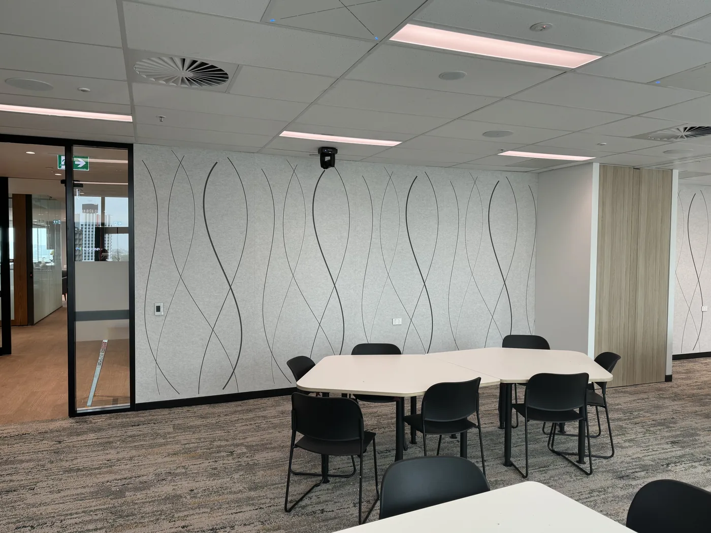 Light acoustic wall with dark wavy ribbon pattern beside a glass meeting room