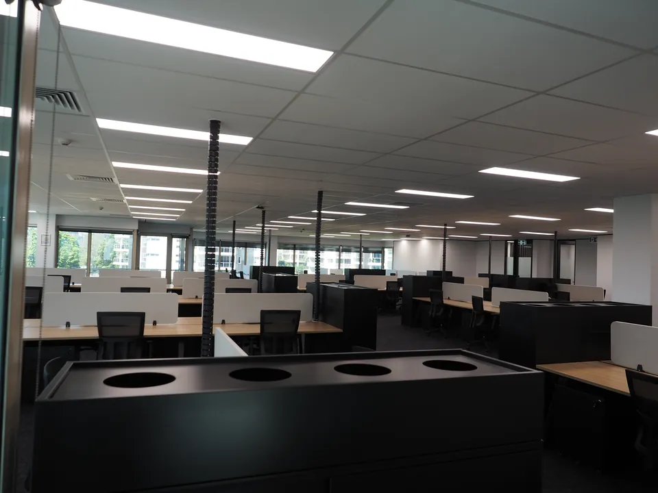 Black tambour unit with planter cut-outs in front of an open-plan floor of workstations and desk screens