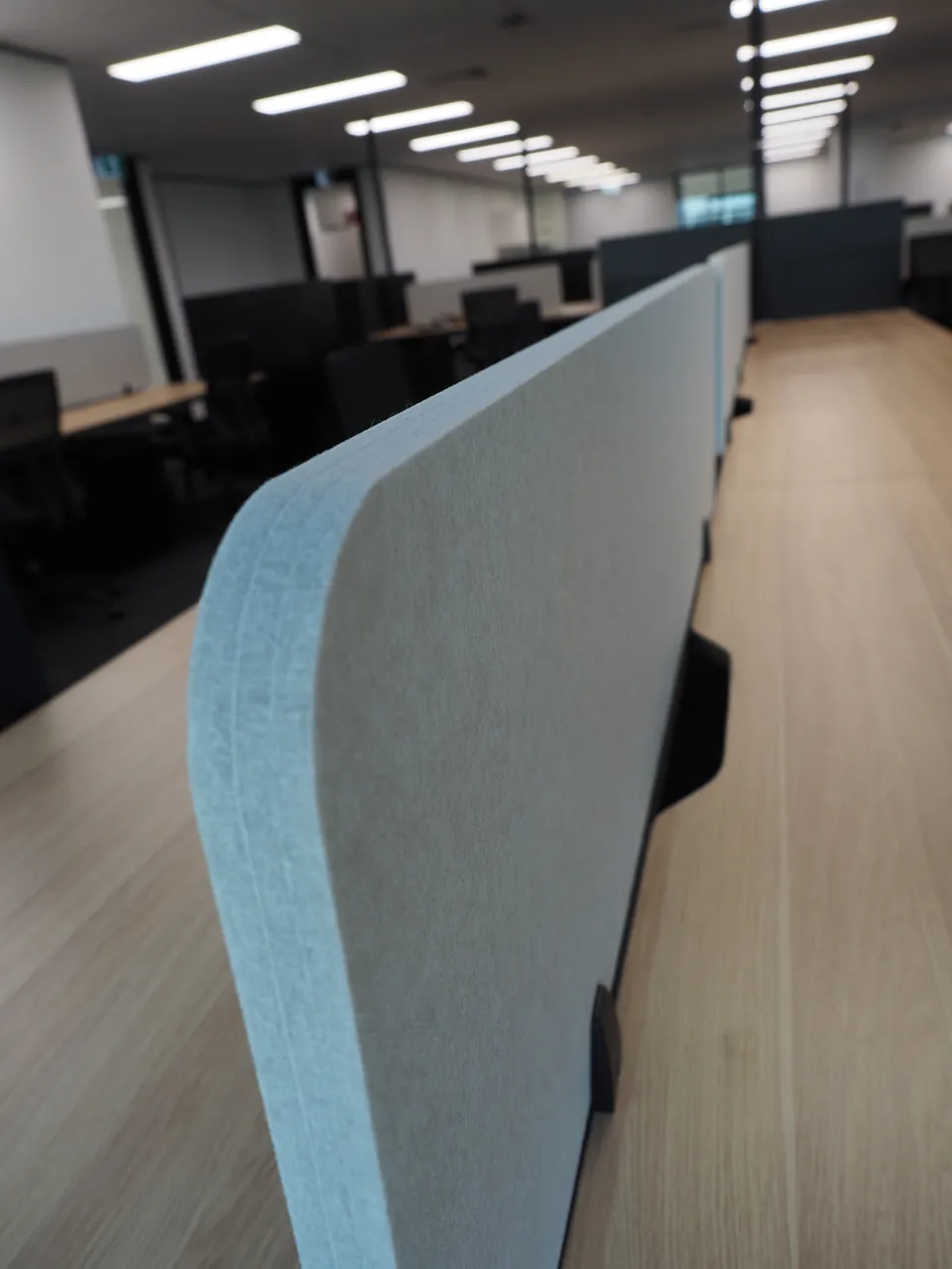 Close-up of a rounded light grey acoustic desk screen fixed to a timber-look workstation
