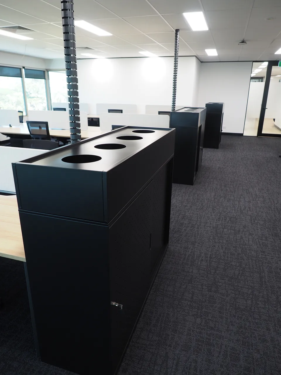 Black tambour units with round planter openings along the end of the workstation rows, with cable risers above