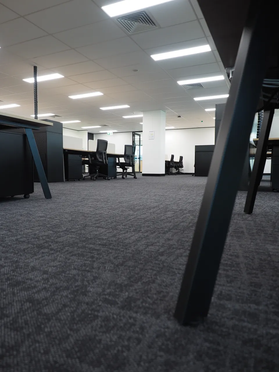 Low view across the carpet to black A-frame workstation legs, pedestals and mesh task chairs