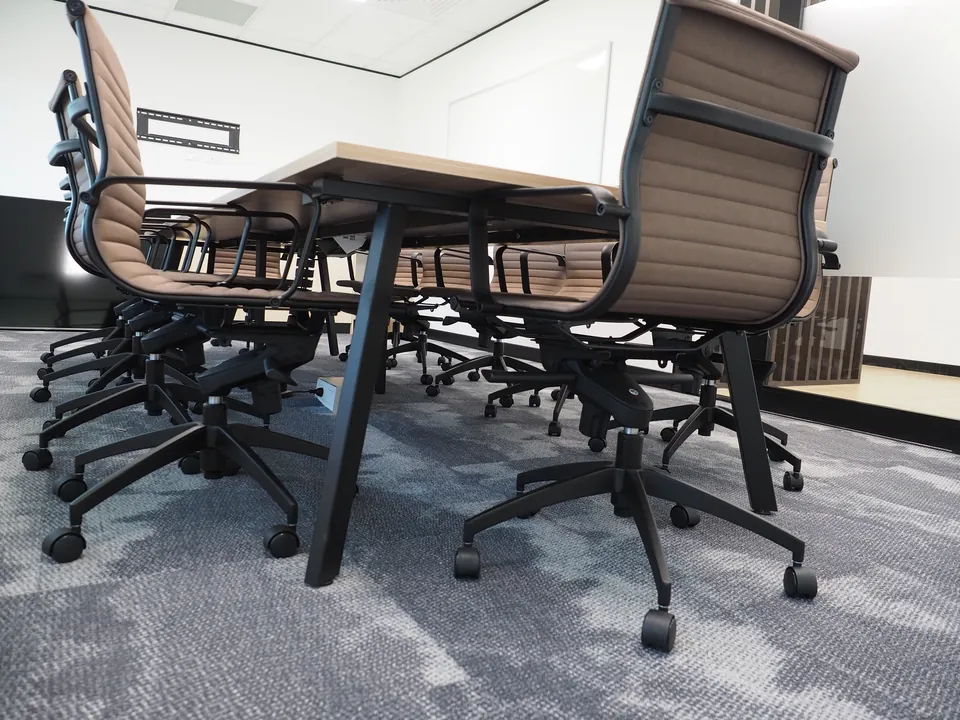 Boardroom table on black A-frame legs with tan ribbed high-back meeting chairs on castors
