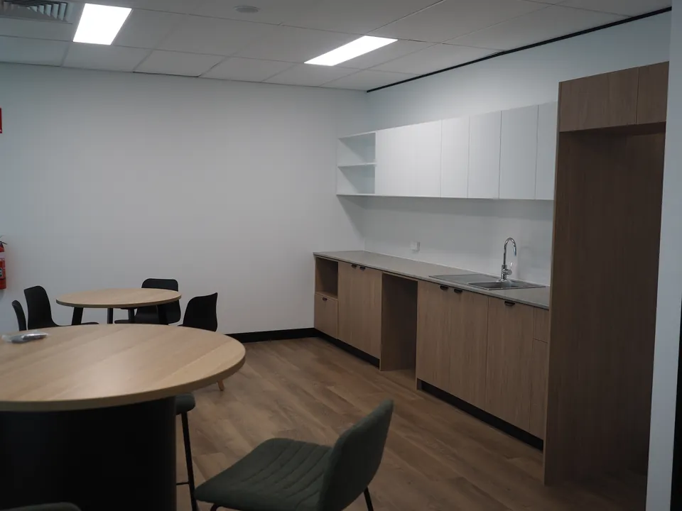 Kitchen and breakout room with round timber-look tables, black chairs and green stools