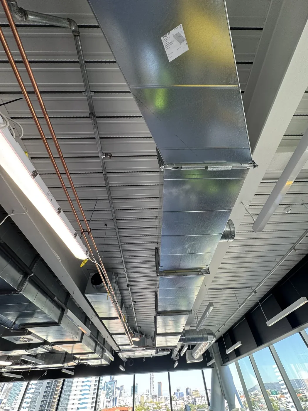 Exposed ceiling ducts and services before acoustic panels — open-plan with city outlook